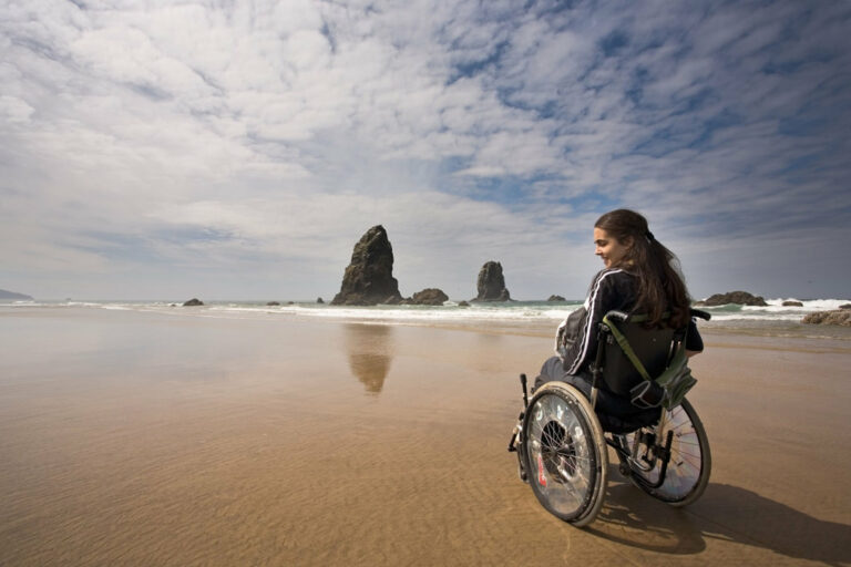 Beautiful young woman in a wheel chair visiting Canon Beach in Oregon, USA.